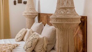 Une chambre à coucher avec une tête de lit en bois, deux décorations murales en macramé et plusieurs coussins.