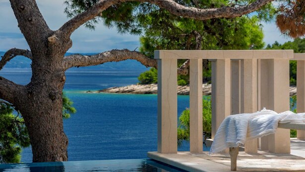 Un espace aménagé au bord de la piscine, avec vue sur la mer, un pergolas et une chaise longue agrémentée d’une serviette blanche.