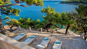 Une terrasse en pierre avec des chaises longues donnant sur la mer.