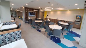 A modern dining area with round tables and chairs, a kitchen area, and a TV screen mounted on the wall. - Microtel Inn & Suites by Wyndham Milford (Milford)