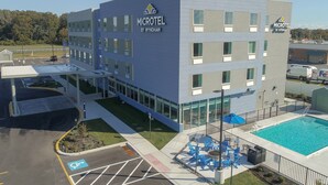 A modern microhotel with a swimming pool, outdoor seating, and a parking area. - Microtel Inn & Suites by Wyndham Milford (Milford)