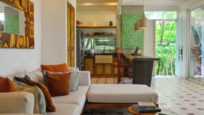 A modern living room with a sofa, ottoman, and a dining area with a kitchen in the background. - In the gated community of Mar-A-Mar, walking distance from La Lora famous surf break and nicest white sand beach, the home counts with 3 bedrooms, 2 bathrooms, nice living room with open space kitchen & terraces. 24/7 security and shared pool. (Playa Santa Teresa de Cobano)