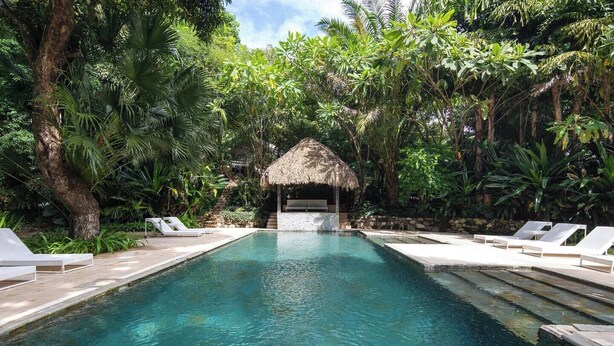 A pool with lounge chairs and a thatched-roof structure surrounded by lush greenery. - In the gated community of Mar-A-Mar, walking distance from La Lora famous surf break and nicest white sand beach, the home counts with 3 bedrooms, 2 bathrooms, nice living room with open space kitchen & terraces. 24/7 security and shared pool. (Playa Santa Teresa de Cobano)
