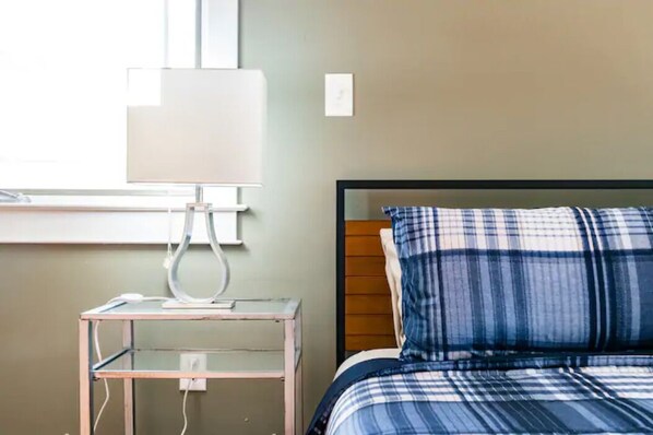 A bedroom with a bed, a bedside table, a lamp, and a window.