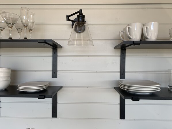 A kitchen with two black shelves, each holding plates, glasses, and a coffee maker. - Alturas 1: New Modern 1BR Cabin, Big Windows for Big Mountain Views (Dillon)