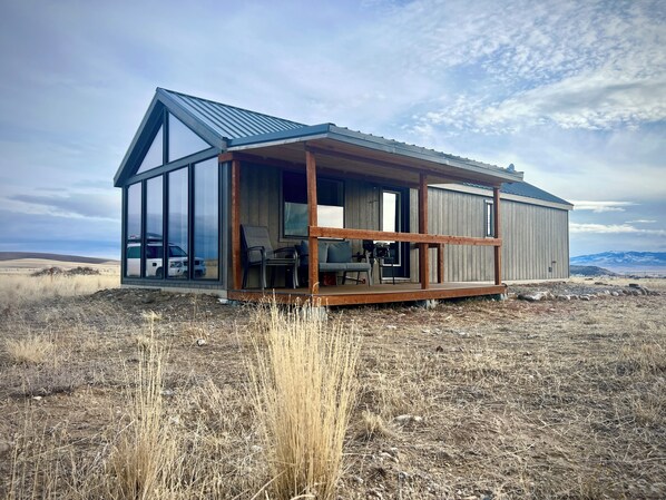 A modern, single-story building with large windows, a wooden deck, and a mountainous backdrop.