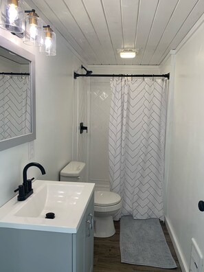 A bathroom with a white sink, black faucet, white toilet, and a shower with a chevron-patterned curtain. - Alturas 1: New Modern 1BR Cabin, Big Windows for Big Mountain Views (Dillon)