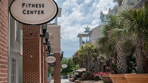 A pathway lined with brick buildings, a 'Fitness Center' sign, and outdoor seating areas with potted plants. - Mid Century Modern meets Beach Chic, Beach views/ pool access,302G Port O Call (Isle of Palms)