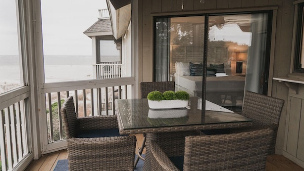 A covered outdoor seating area with wicker furniture and a glass table, overlooking a residential area. - Mid Century Modern meets Beach Chic, Beach views/ pool access,302G Port O Call (Isle of Palms)
