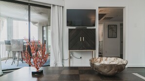 A modern living room with a large flat-screen TV, a dark wooden cabinet, and a unique sculptural centerpiece. - Mid Century Modern meets Beach Chic, Beach views/ pool access,302G Port O Call (Isle of Palms)