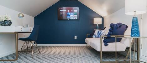 Una habitación moderna con una pared de acento azul oscuro, un televisor montado, un escritorio con una silla, una cama con ropa de cama azul y un suelo estampado.