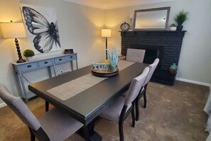 Un coin repas comprenant une table, des chaises, une lampe, une cheminée et une horloge murale.