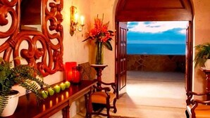 A lobby with a wooden reception desk, a vase with flowers, and a view of the ocean through an open door. - Gorgeous 3BR Villa Perfect View at Cabo San Lucas (Cabo San Lucas)