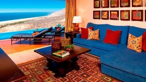 A living room with a blue sofa, red cushions, a coffee table with books, and a view of the ocean. - Gorgeous 3BR Villa Perfect View at Cabo San Lucas (Cabo San Lucas)