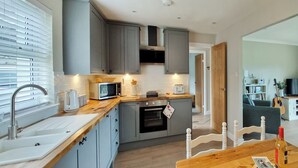 A modern kitchen with grey cabinets, a wooden countertop, a built-in oven, and a dining area with a wooden table and chairs. - 2 bedroom accommodation in Tayvallich (Tayvallich)
