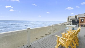 Vista de una playa con muelle de madera, sillas amarillas y un edificio con balcones.