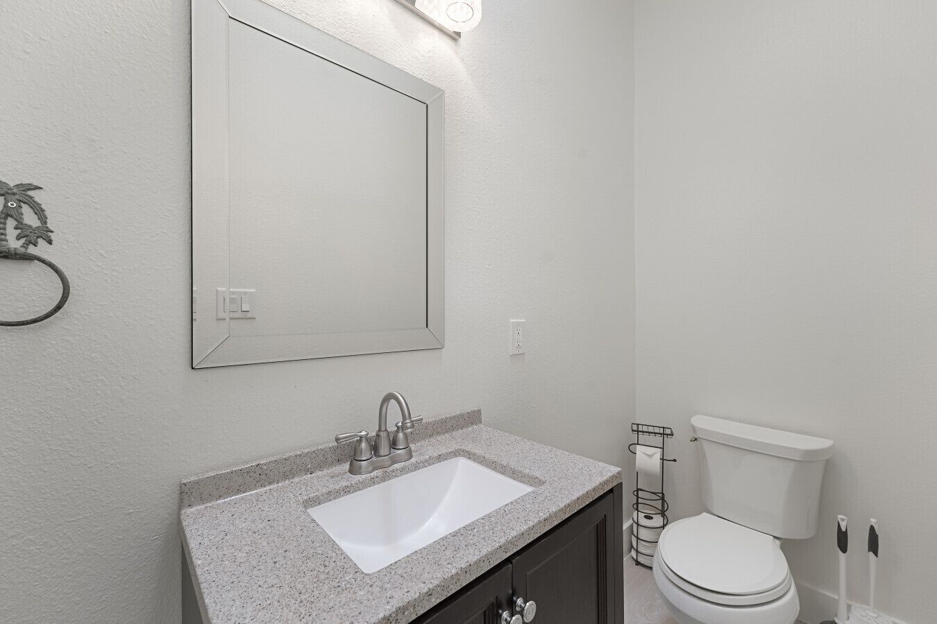 Un baño con lavamanos blanco, espejo, inodoro y toallero.