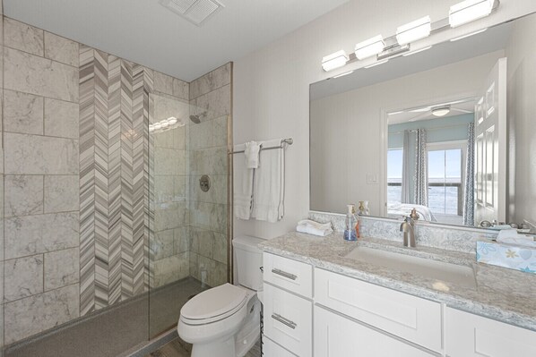 A bathroom with a shower, toilet, vanity, and a large mirror.