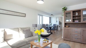 Ett modernt vardagsrum med en soffa, ett soffbord med blommor, en matplats med stolar och ett köksområde med skåp.