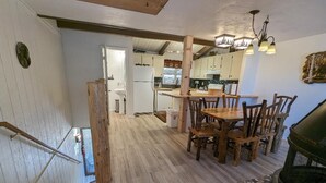 A rustic interior with a wooden dining table and chairs, a fireplace, and a kitchen in the background. - Your All-Season Chalet Basecamp – A/C + Unmatched Location! (Big Bear Lake)