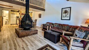 A spacious living area with a high ceiling, a wooden staircase, a fireplace, and a cozy seating arrangement. - Your All-Season Chalet Basecamp – A/C + Unmatched Location! (Big Bear Lake)