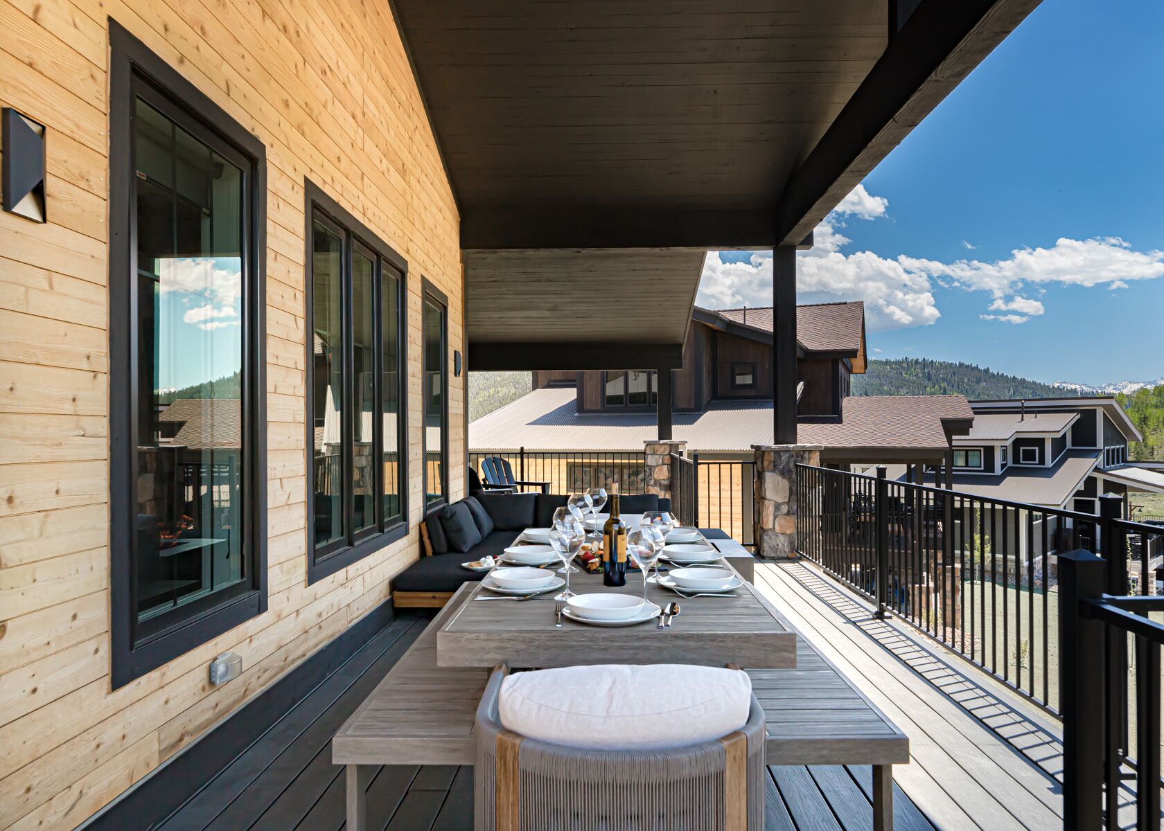 A wooden deck with a dining table set for four, large windows, and a view of a mountain landscape.