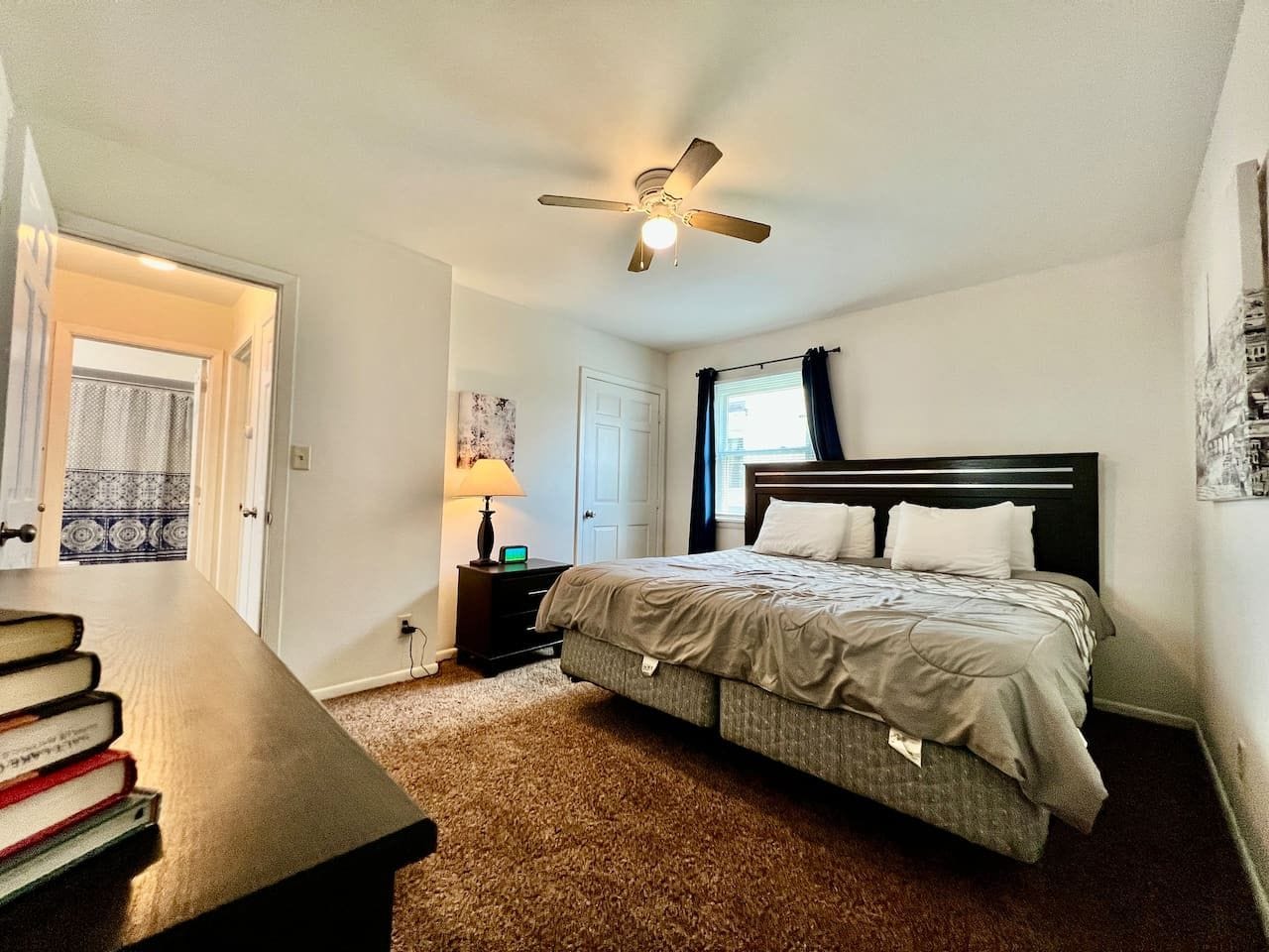 A bedroom with a bed, a nightstand, a lamp, a ceiling fan, and a door leading to another room.