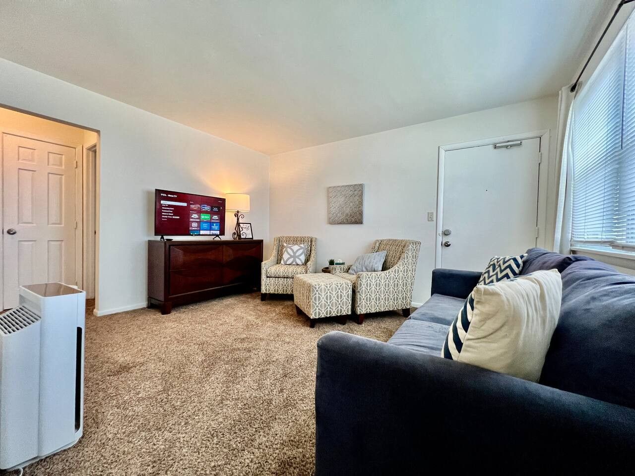 A living room with a dark sofa, two patterned armchairs, a wooden cabinet, and a TV.