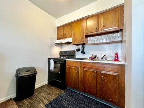 Una cocina compacta con armarios de madera, una estufa negra y un cubo de basura.