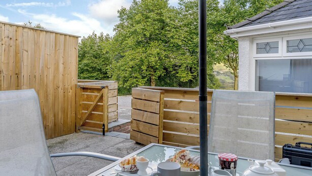 An outdoor seating area with a table set for two, a wooden fence, and a building with windows in the background. - Rural romantic getaway for two. (Neath)