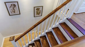 A staircase with wooden steps and white railings, leading to a landing with framed artwork on the wall. - Rural romantic getaway for two. (Neath)