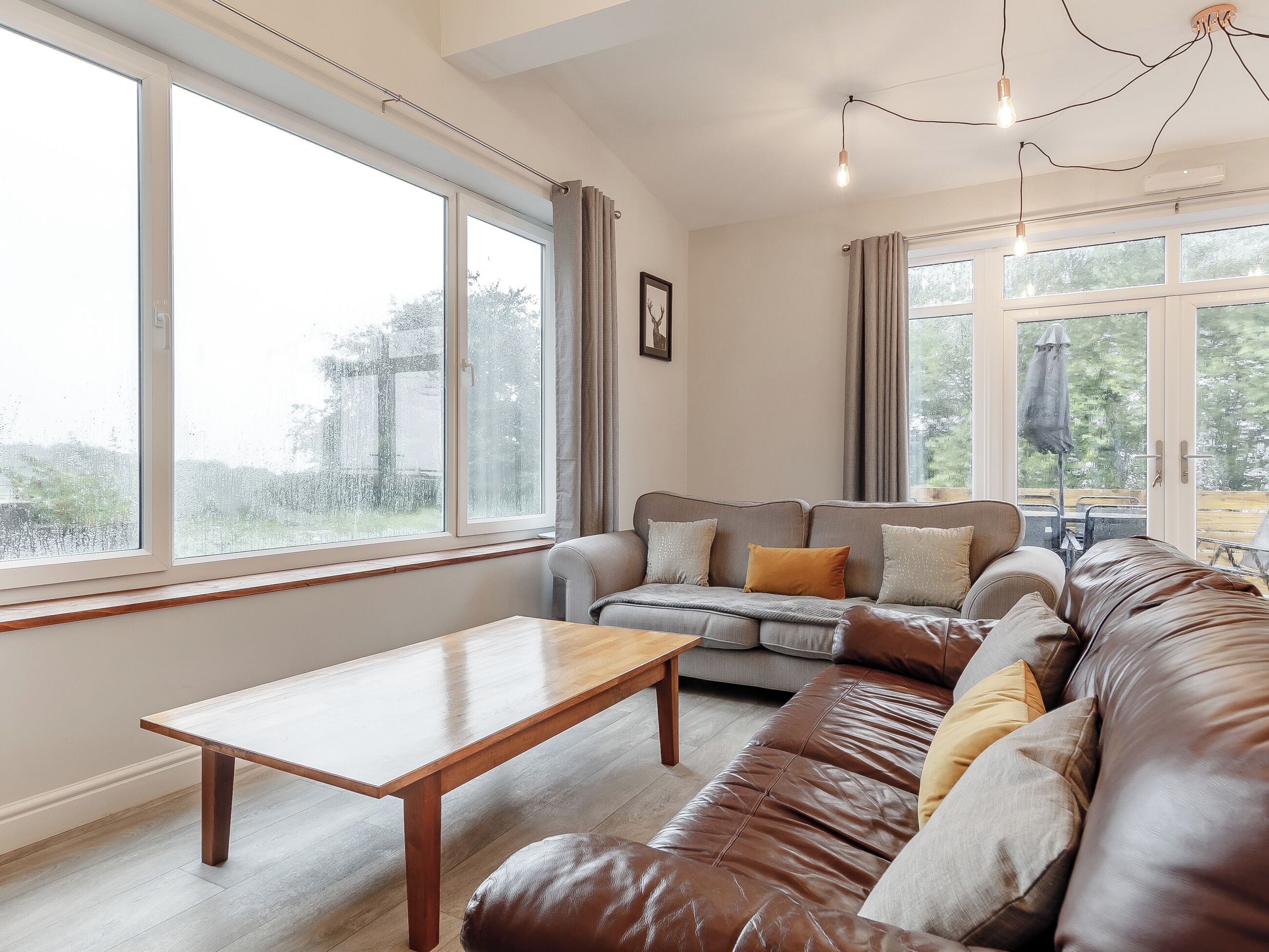 A living room with a sofa, a wooden coffee table, and large windows.