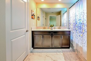 A bathroom with a double sink, dark cabinets, a marble floor, and a shower curtain with a geometric pattern.
