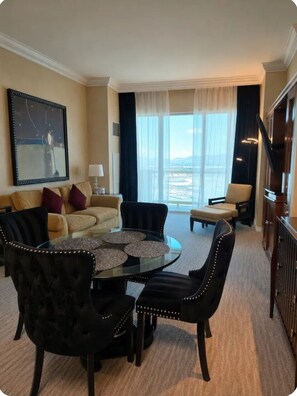 A hotel room with a dining area, a sofa, a large window with a view, and a staircase.