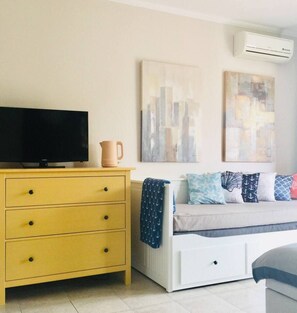 A room with a yellow dresser, a white sofa with patterned cushions, and abstract wall art.