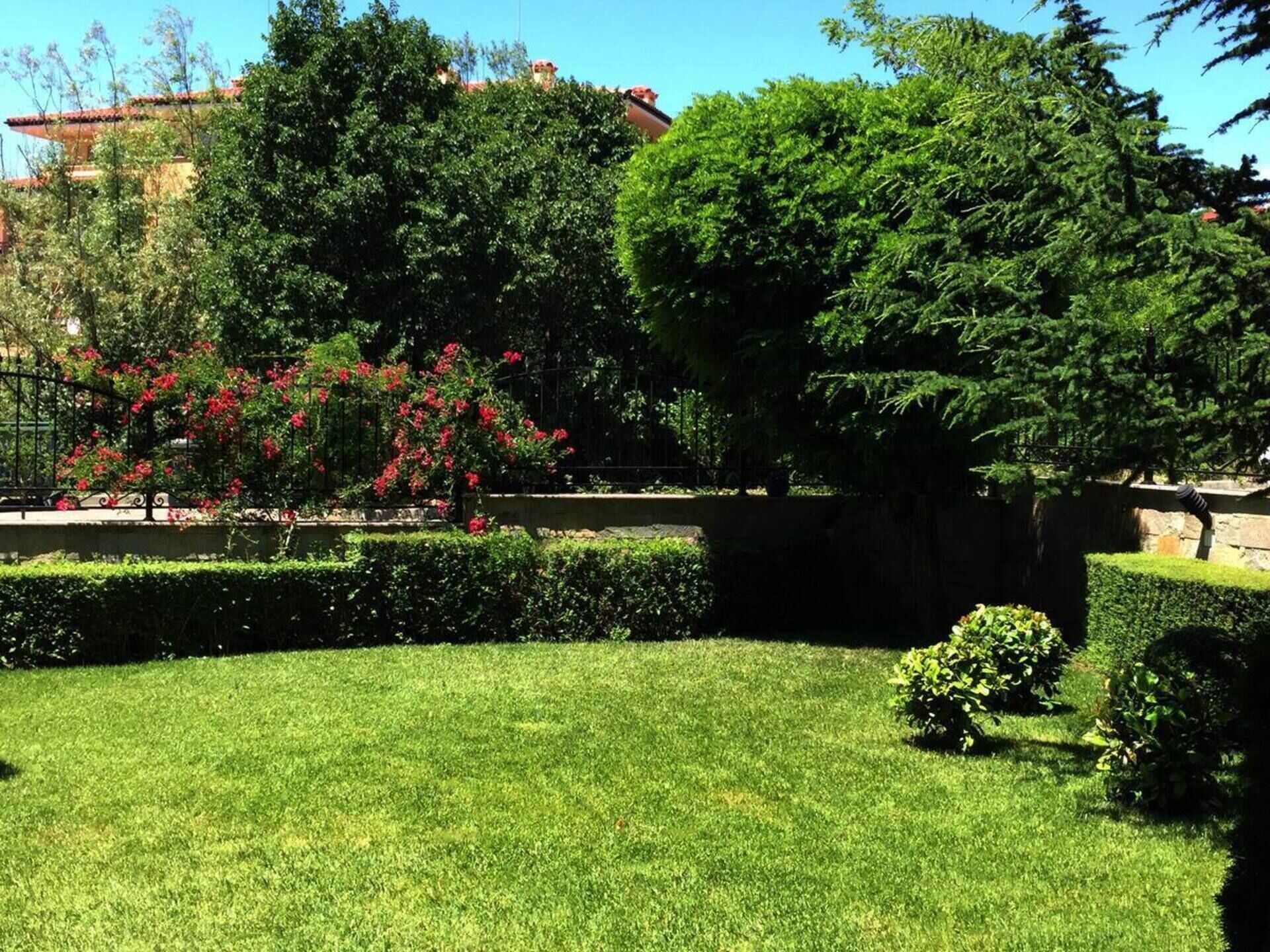 A well-maintained garden with manicured lawns, a variety of trees, and flowering shrubs.