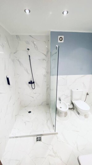 A modern bathroom with a glass-enclosed shower, white marble tiles, a toilet, and a bidet.