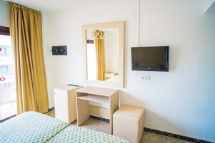 Una habitación de hotel con cama, escritorio, espejo, televisor y ventana con cortinas.