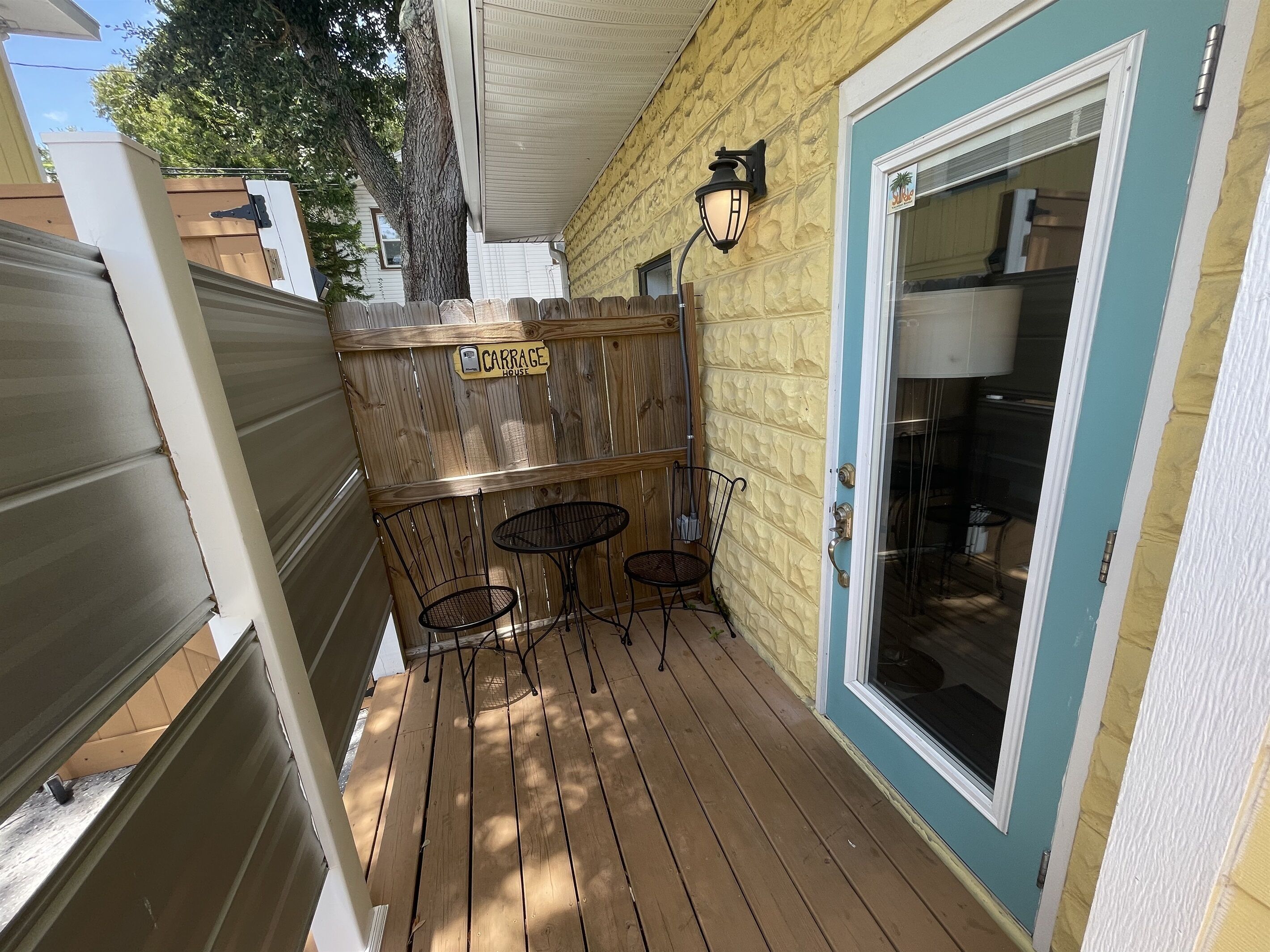 A wooden deck with two metal tables and chairs, a wooden fence, and a door with a window.