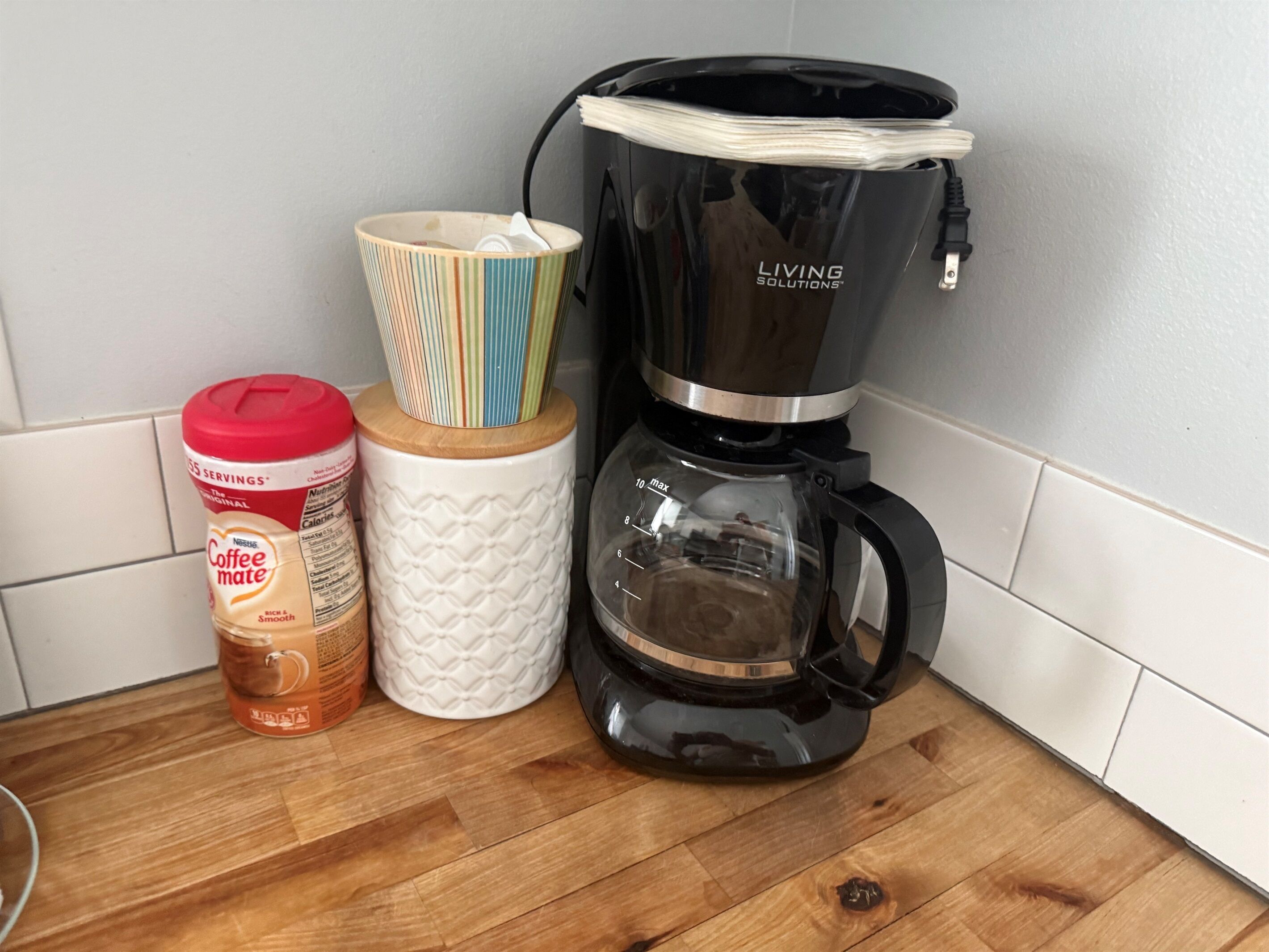 A kitchen counter with a coffee maker, a jar of coffee creamer, and a striped mug.
