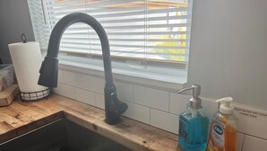Una cocina con un grifo negro, un escurreplatos y dos dispensadores de jabón en la encimera.