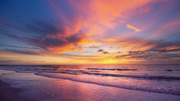 Una playa al atardecer con olas y un cielo colorido.