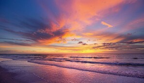 A beach at sunset with waves and a colorful sky.