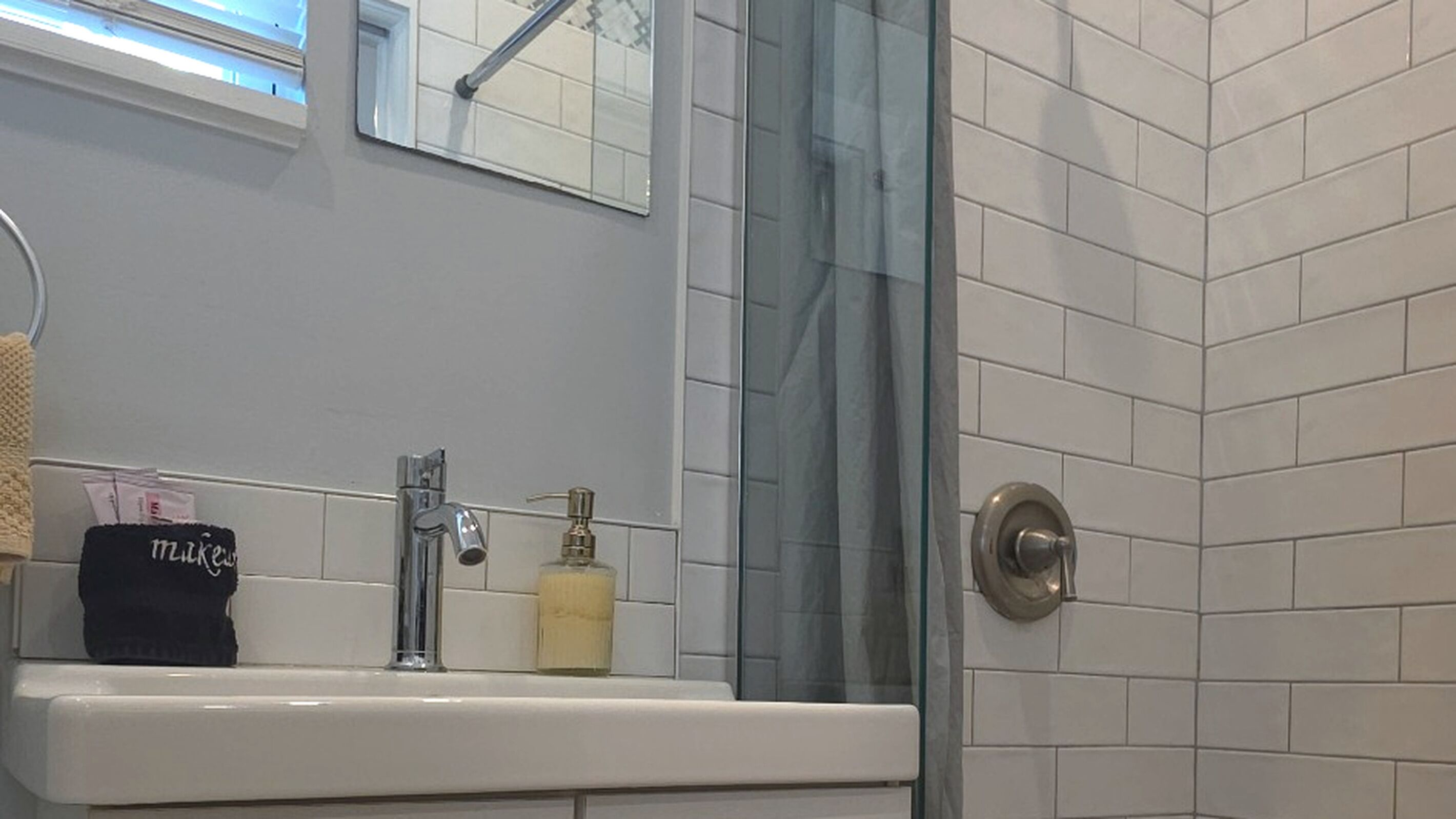 A bathroom with a white sink, a mirror, a shower with a glass door, and a towel rack.