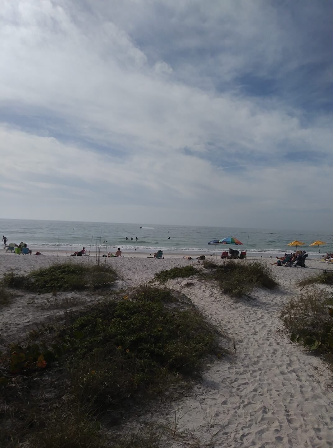 A beach with sand, sparse vegetation, and a cloudy sky.