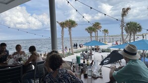 Un restaurant en bord de mer avec une terrasse, des palmiers et une vue sur l’océan.