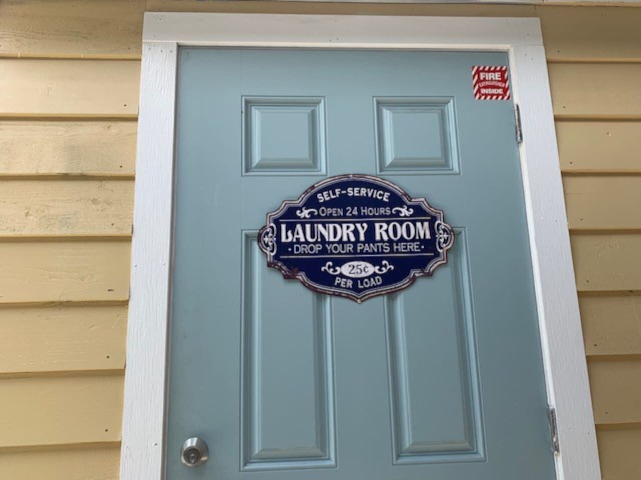A door with a sign indicating a self-service laundry room open 24 hours, with a 25c charge per load.