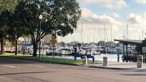 Un port de plaisance avec des bateaux amarrés, une promenade piétonne et un espace vert agrémenté d’arbres et de bancs.