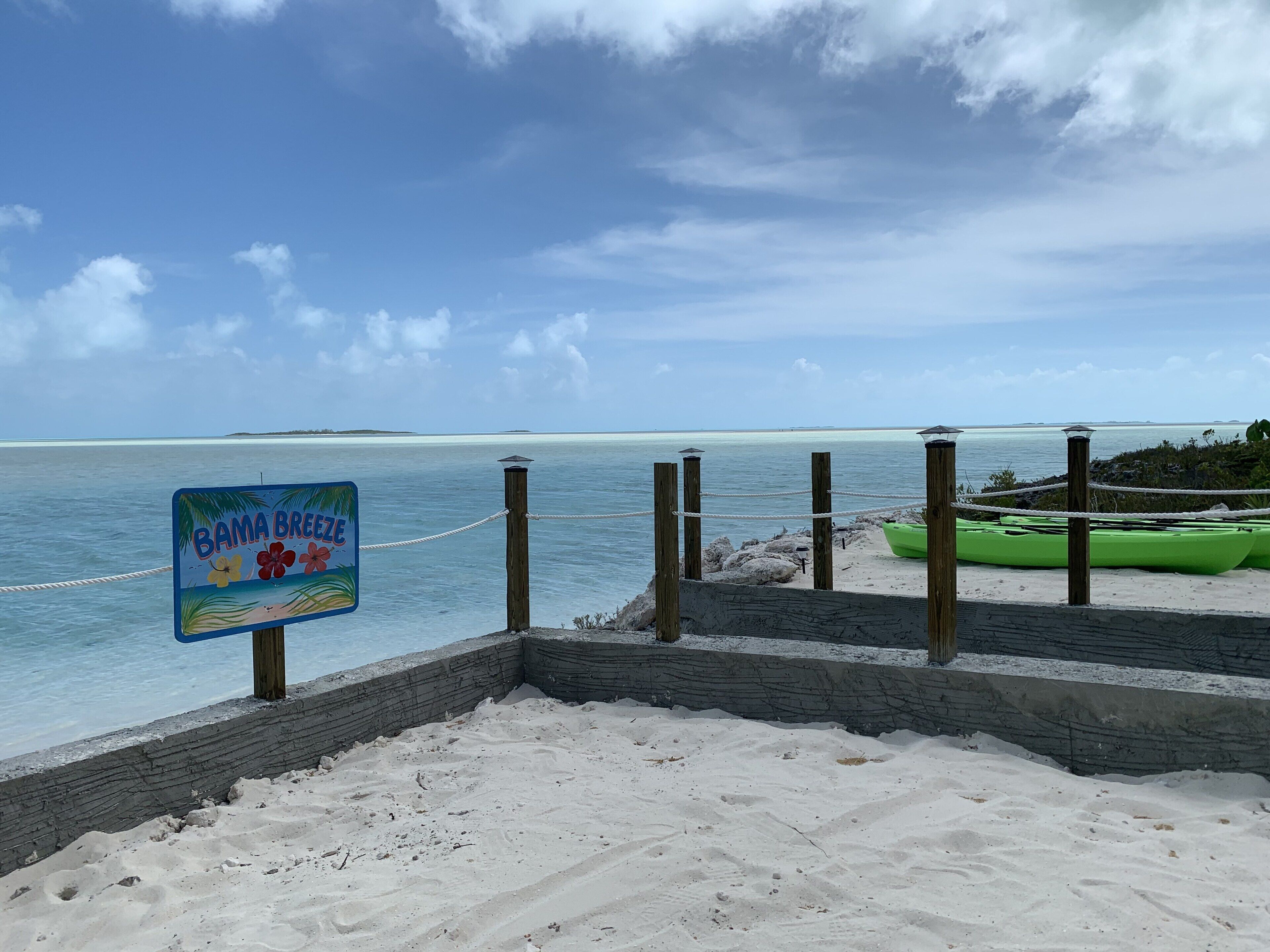 A beach with a sign reading "BAMA BREEZE" and a green kayak on the sand.