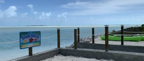 A beach with a sign reading "BAMA BREEZE" and a green kayak on the sand.